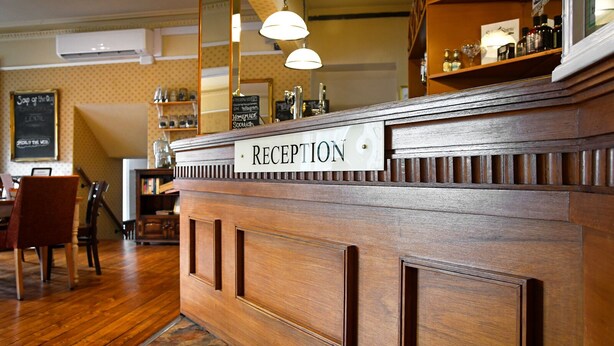 A reception desk with a sign, wooden paneling, and a tiled floor. - Corner House Hotel (Annan)