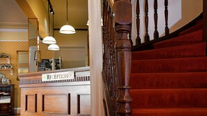 A reception desk with a sign reading "RECEPTION" and a staircase with wooden balusters. - Corner House Hotel (Annan)