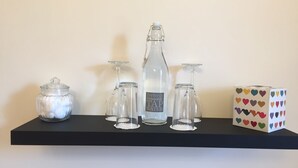 A shelf with a glass bottle labeled "Perfectly Drinkable TAP WATER," two glass carafes, a glass jar, and a box with a heart pattern. - The Village Inn and Kirtle House B&B (Lockerbie)
