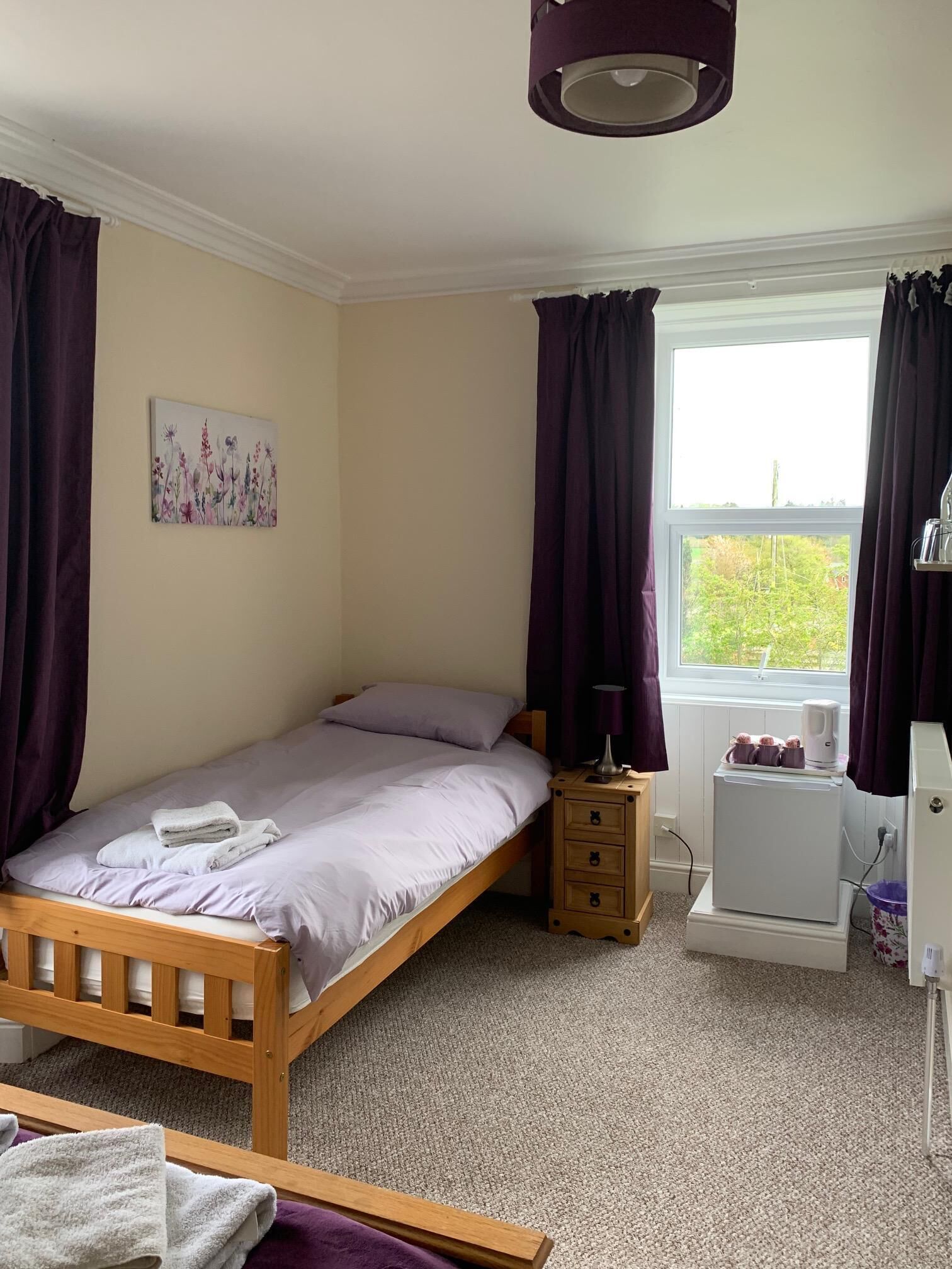 A bedroom with a single bed, a bedside table, a heater, and a window with curtains.