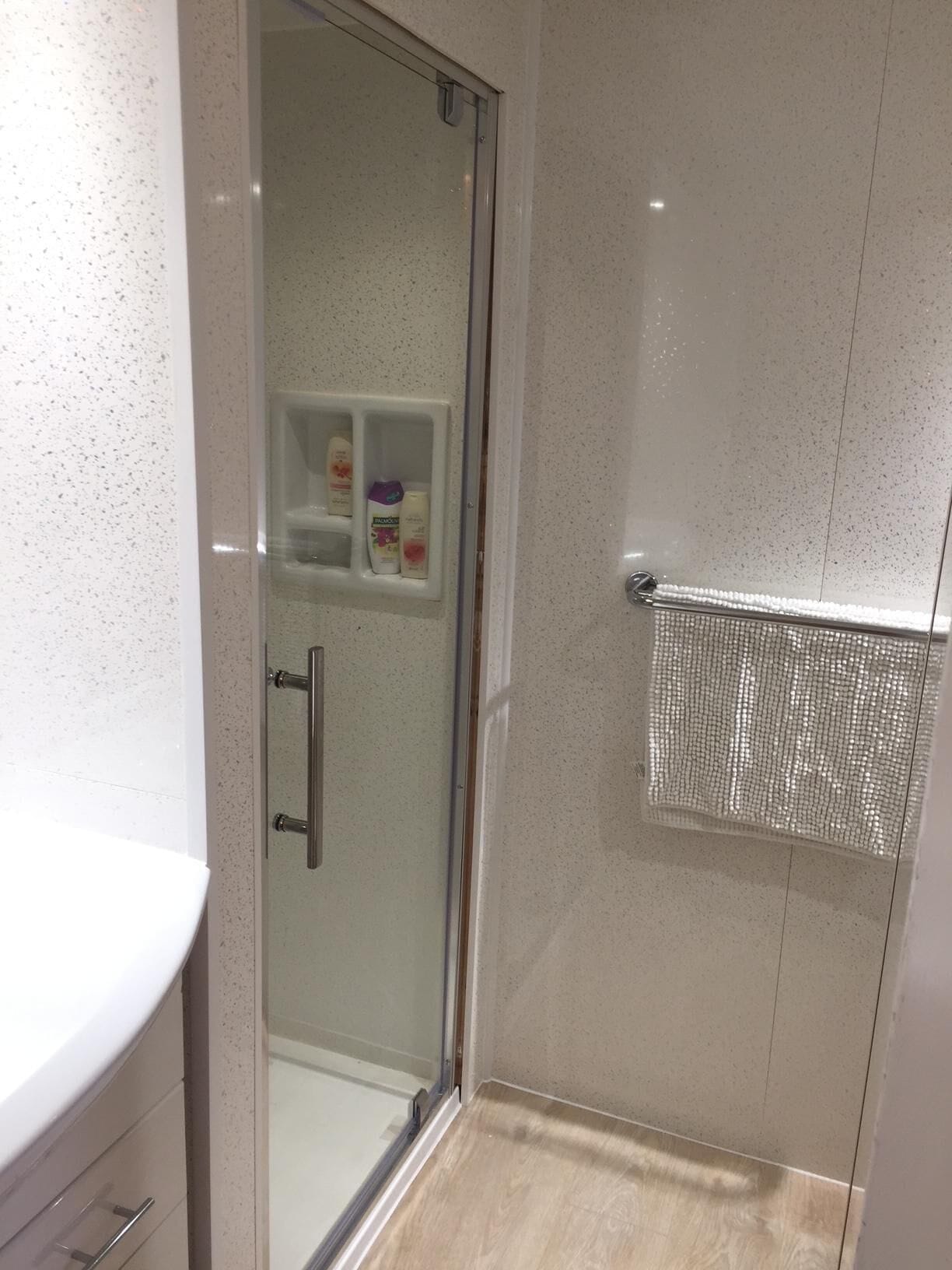 A modern bathroom with a glass shower enclosure, a white sink, and a small shelf with toiletries.