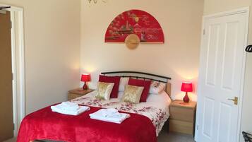 Una cama bien hecha con una manta y almohadas rojas, dos lámparas de noche y una obra de arte colgada en la pared sobre la cama.