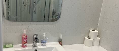 Un baño con lavamanos blanco, un espejo, inodoro y cabina de ducha.