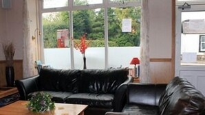 A room with a black leather sofa, a wooden coffee table, and a window with a view of greenery. - The Village Inn and Kirtle House B&B (Lockerbie)