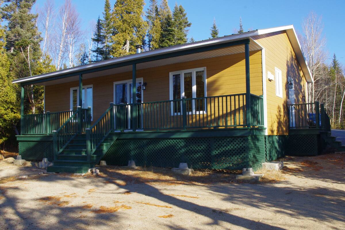 Eine zweistöckige Lodge mit einer grünen Veranda und mehreren Fenstern.