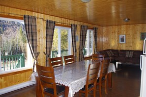 Ein Holzinterieur mit einem für vier Personen gedeckten Esstisch, einer Couch und großen Fenstern mit karierten Vorhängen.