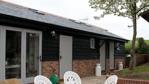 A house with a brick exterior, a black roof, and a sliding glass door. There are outdoor chairs and a green hose visible.