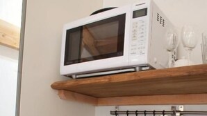 A kitchen with a microwave on a wooden shelf, a stainless steel sink, and hanging utensils.