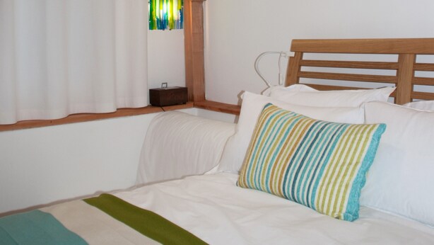A bed with white bedding and a striped pillow, a wooden headboard, and a window with curtains.