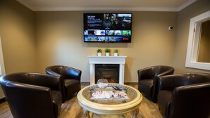 Una sala de estar con chimenea, sillones de cuero, una mesa de centro de vidrio y un televisor de pantalla plana montado en la pared.