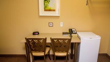 A small office with a desk, two chairs, a refrigerator, a phone, a clock, and a framed picture on the wall.