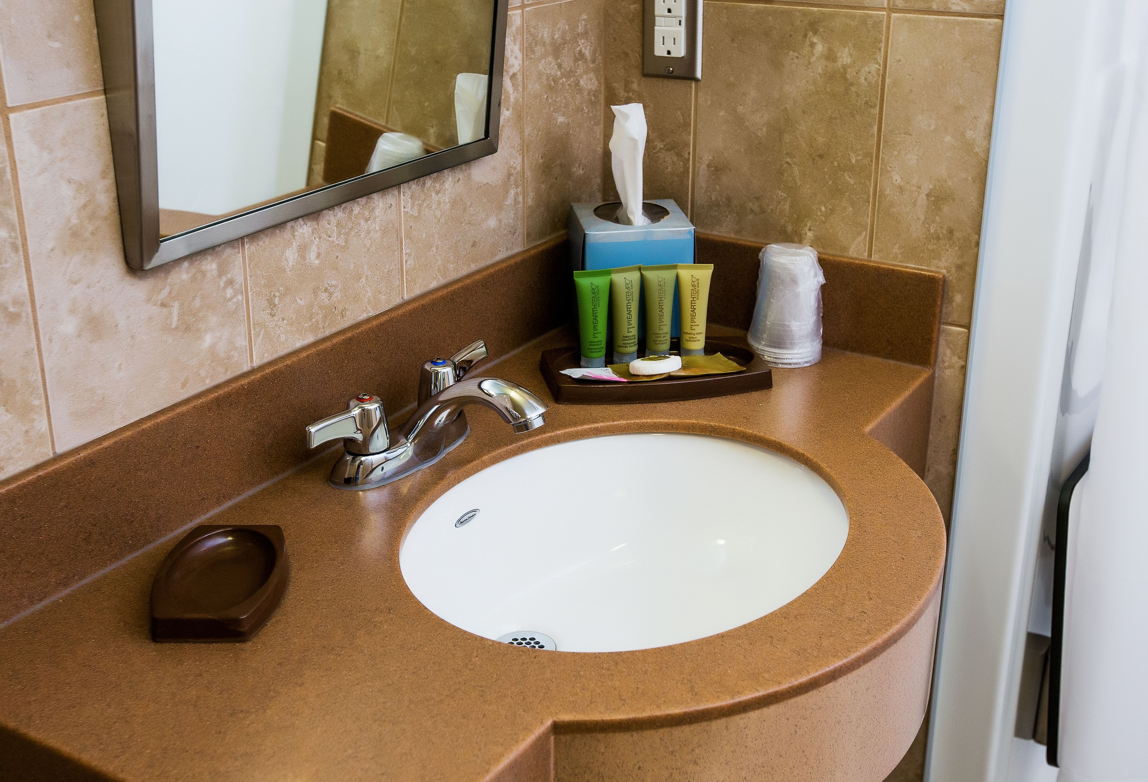 A bathroom sink with a mirror, a soap dish, and toiletries.