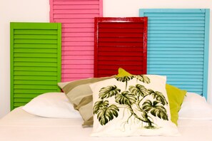 Un lit avec des oreillers et des volets aux couleurs vert, rose, rouge et bleu.