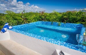 A pool with blue mosaic tiles, surrounded by lush greenery.