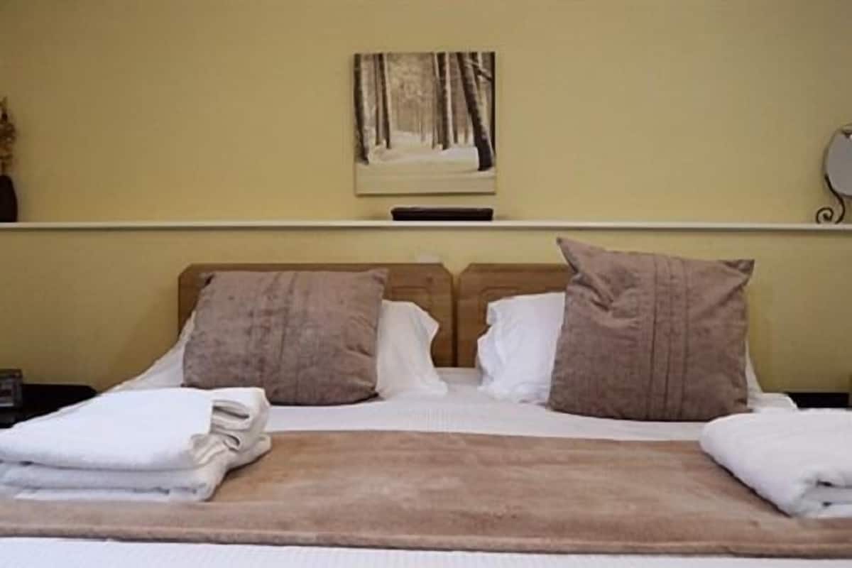 Quarto de hotel com cama, almofadas, cobertor e uma pintura na parede.