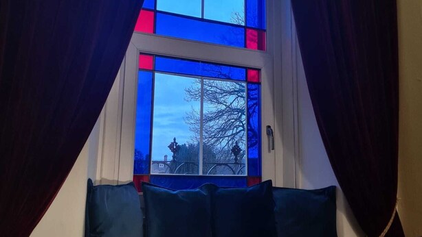 A room with a window featuring blue-tinted glass panes and dark curtains.