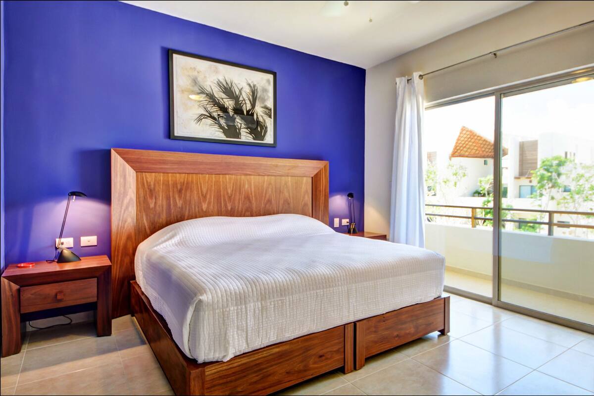 Une chambre à coucher avec un lit en bois, une table de chevet, une lampe et un tableau encadré au mur.