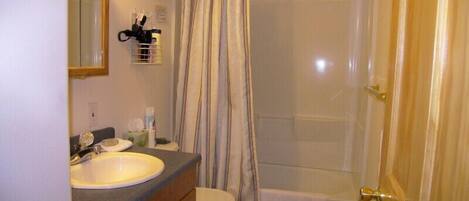 A bathroom with a sink, toilet, shower, and a wooden door.