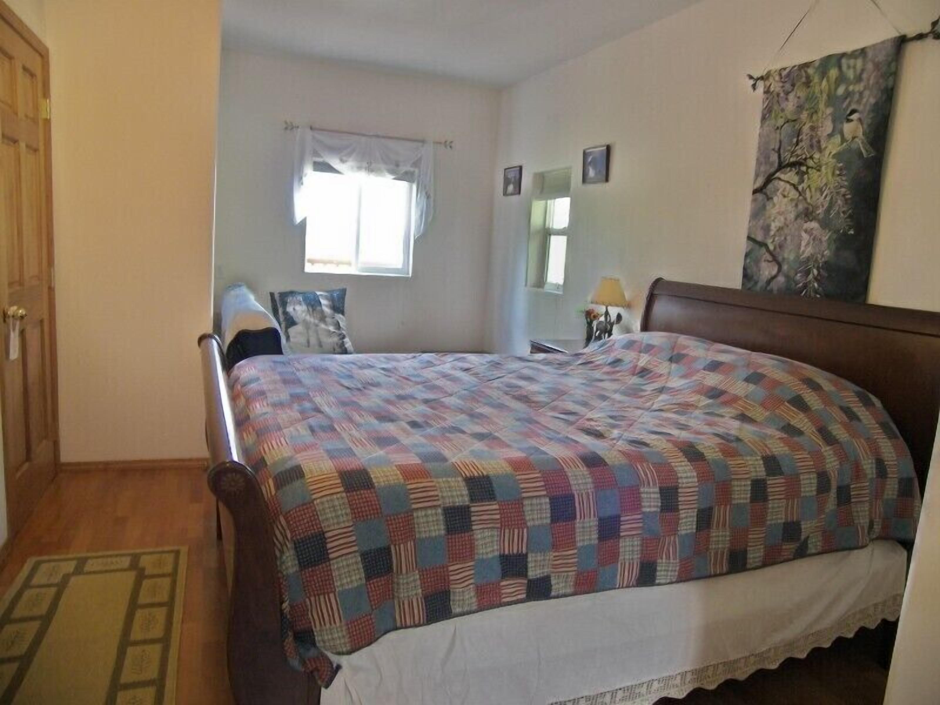A bedroom with a bed, a window with curtains, a wooden door, and a wall-mounted lamp.