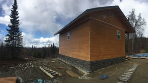 A wooden cabin with a stone foundation, surrounded by a forest. - Grace and Bill's Freedom Hills (Talkeetna)