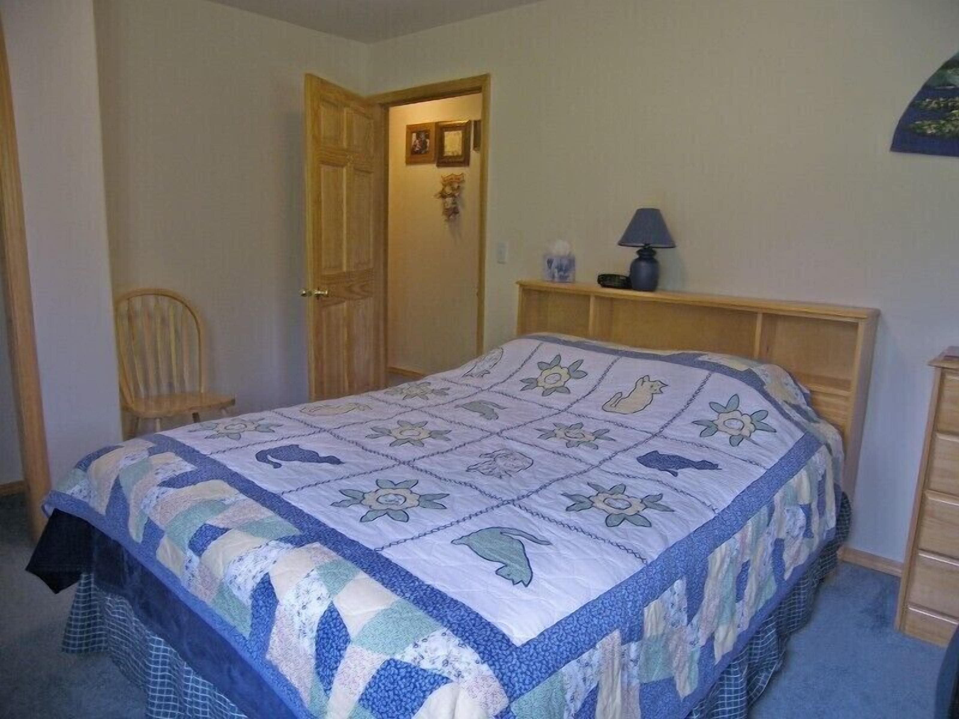 A bedroom with a bed, a chair, a wooden door, and a nightstand with a lamp.