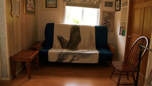 A cozy living room with a sofa covered in a bird-themed blanket, a wooden coffee table, and a wooden chair. - Grace and Bill's Freedom Hills (Talkeetna)