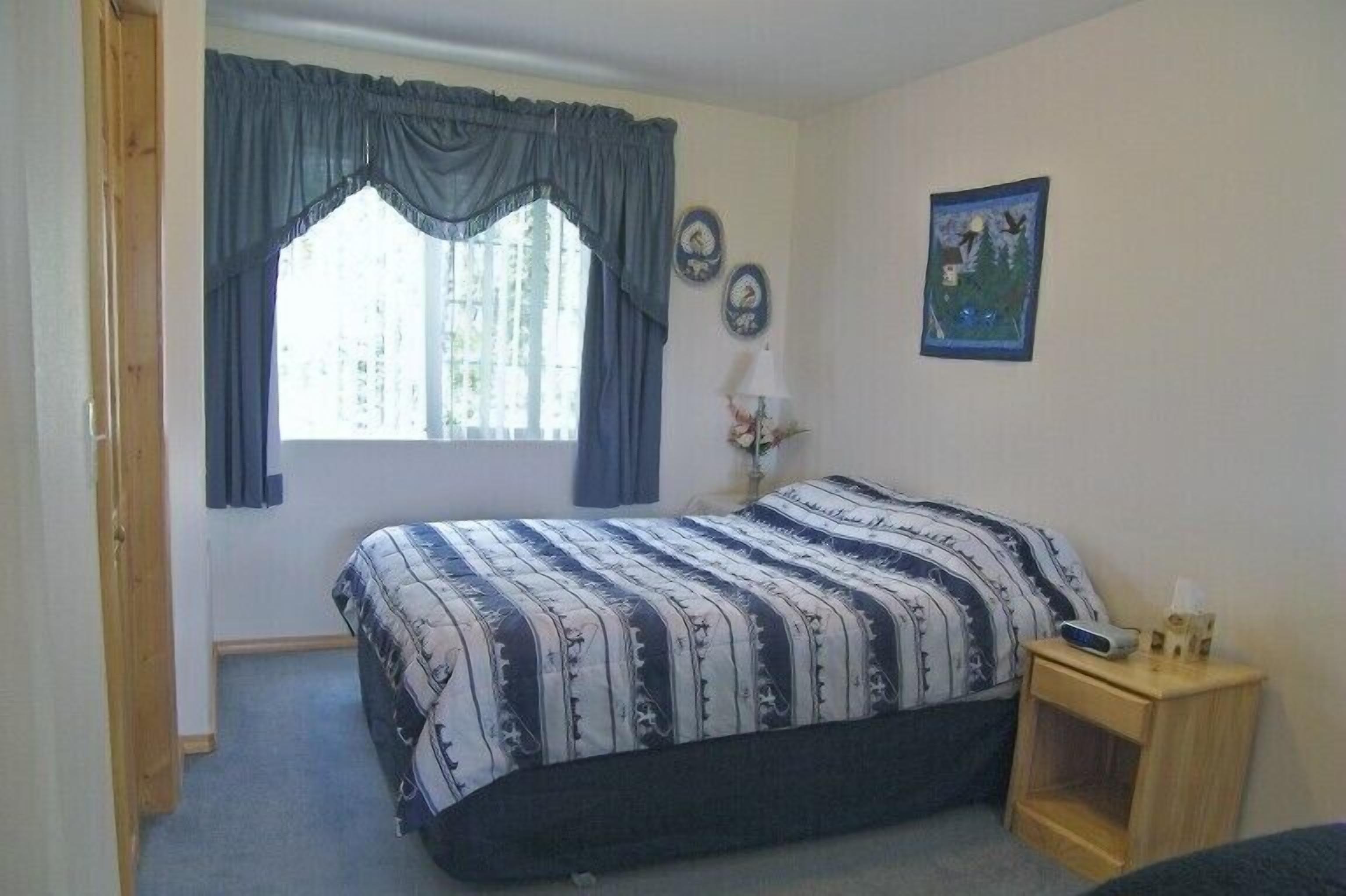 Een slaapkamer met een bed, een raam met gordijnen, een nachtkastje met een lamp, en een klok aan de muur.