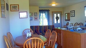 A cozy kitchen with wooden cabinets, a dining table with chairs, and a window with curtains. - Grace and Bill's Freedom Hills (Talkeetna)