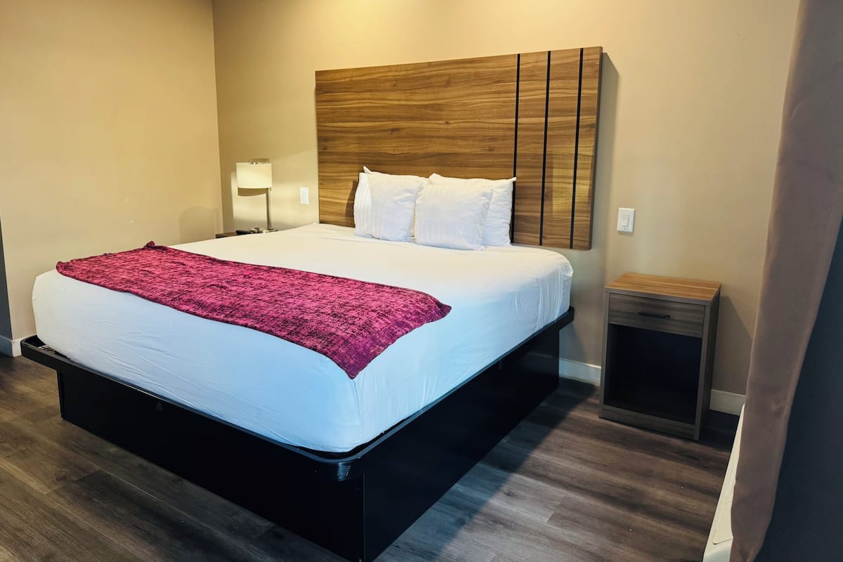 A modern hotel room with a large bed, a wooden headboard, a bedside table, and a nightstand.