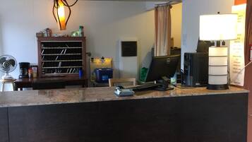 Een hotel receptie met een houten balie, een bureau met een computer, een ventilator en een luchtverkoeler aan de muur.