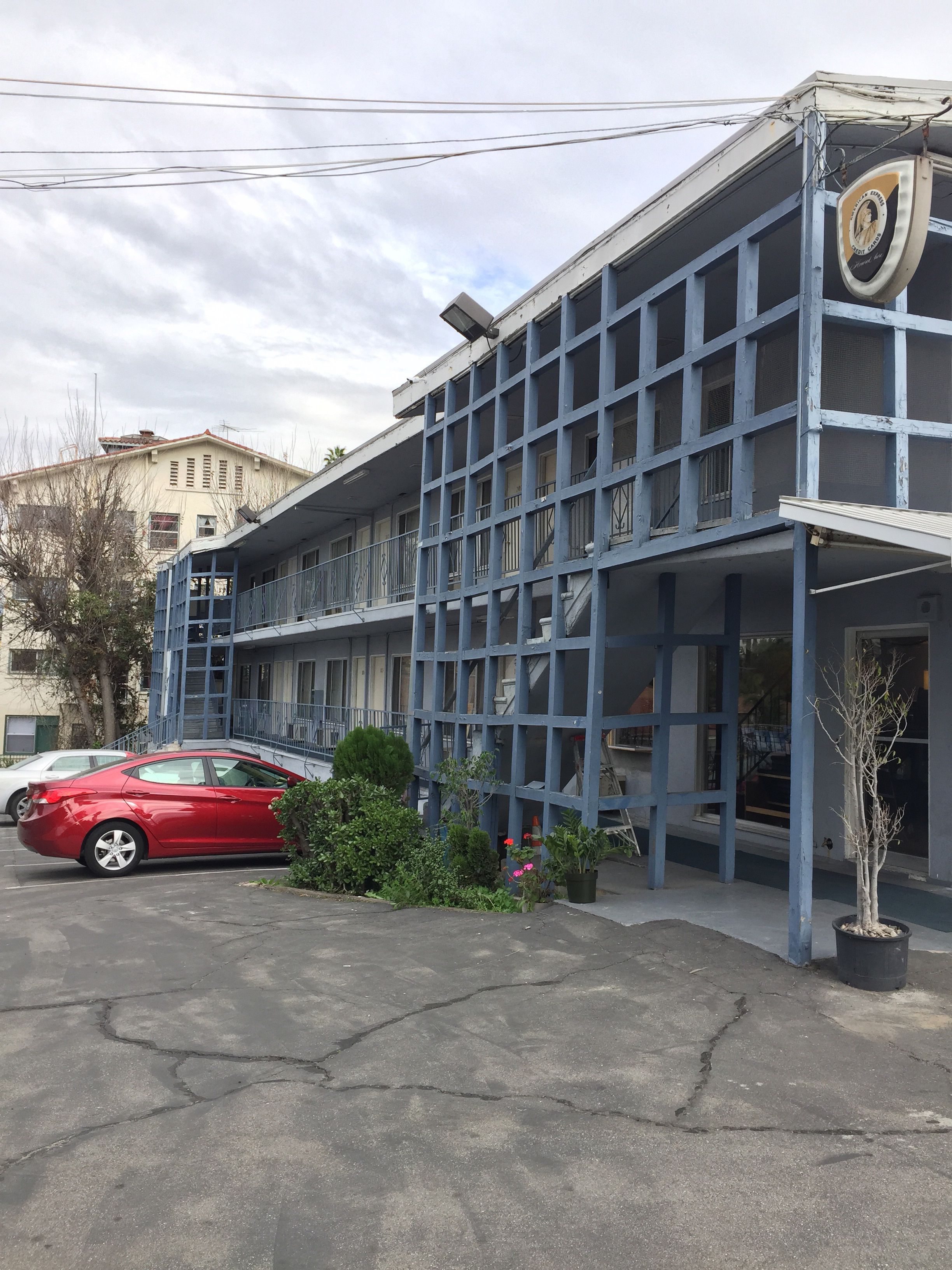 A multi-story building with a blue facade, a red car parked in front, and a small tree in a planter.