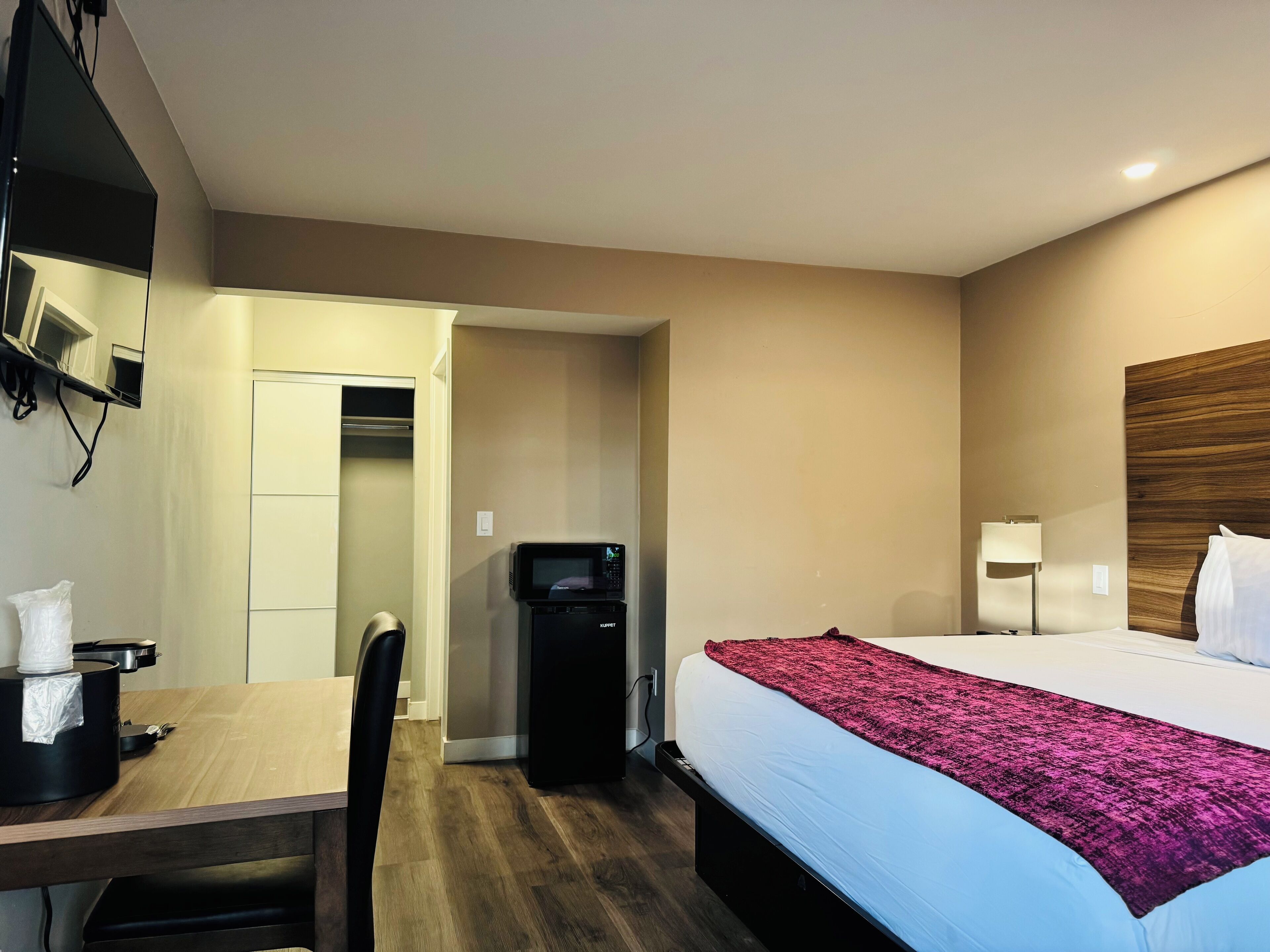 A hotel room with a bed, a desk, a chair, a microwave, and a TV mounted on the wall.
