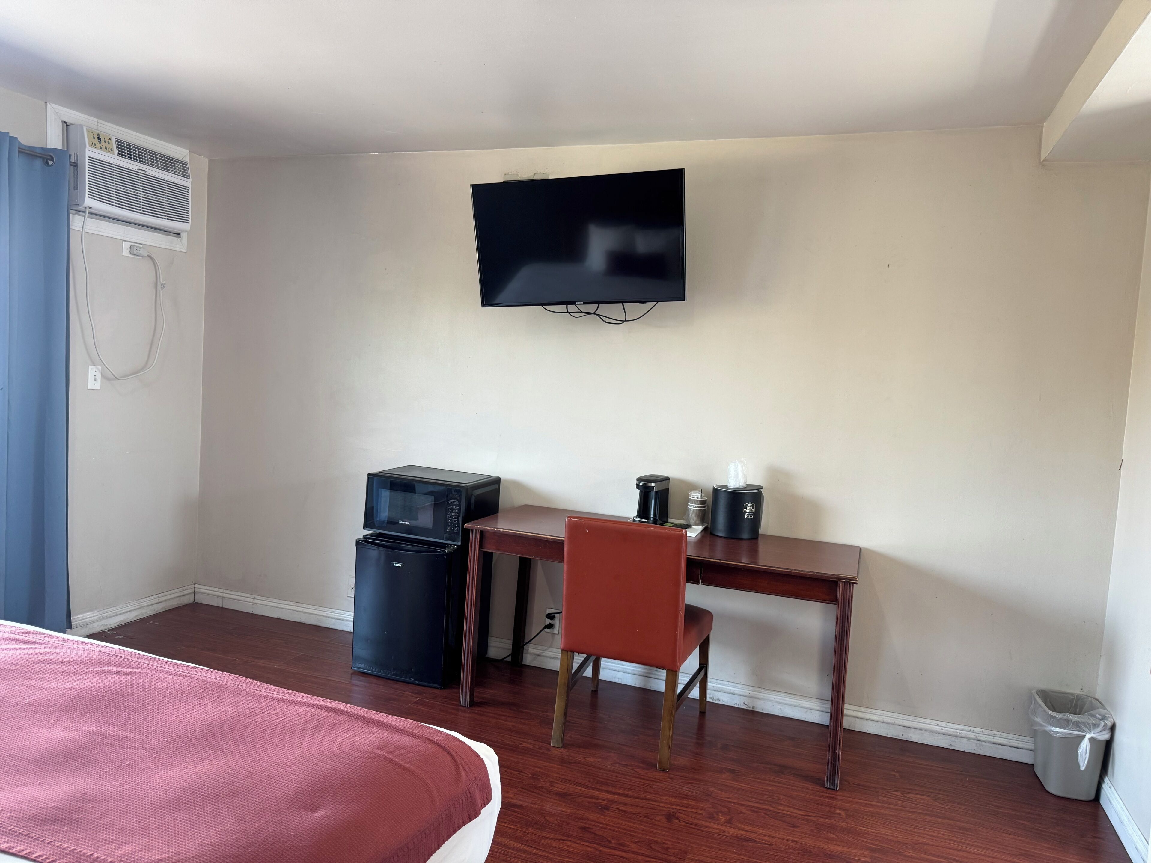 A hotel room with a bed, a desk, a chair, a TV, a microwave, a coffee maker, and a trash bin.
