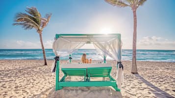 Una playa con cama con dosel, palmeras y el océano.