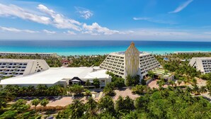A resort with a central building surrounded by lush greenery and a view of the ocean. - The Pyramid Cancun by Oasis - Gourmet Premium All Inclusive (Cancun)