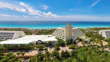A resort with a central building surrounded by lush greenery and a view of the ocean.