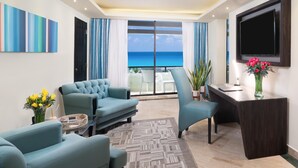A modern living room with a sofa, armchair, and a desk with a TV. There is a large window with a view of the ocean. - The Pyramid Cancun by Oasis - Gourmet Premium All Inclusive (Cancun)