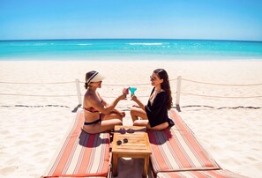 Two people sitting on a striped beach mat with a wooden table between them, facing the ocean. - The Pyramid Cancun by Oasis - Gourmet Premium All Inclusive (Cancun)