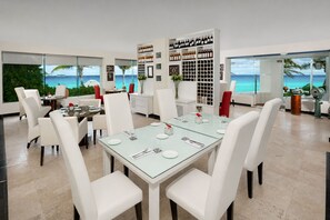 A dining area with a glass table, white chairs, and a view of the ocean. - The Pyramid Cancun by Oasis - Gourmet Premium All Inclusive (Cancun)