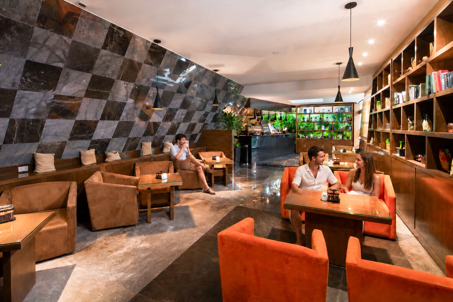 A modern lounge area with seating and a coffee bar, featuring a checkered wall and wooden shelves with books.