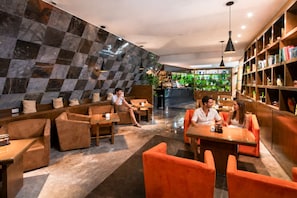 Un moderno espacio de relax con asientos y una barra de café, destacando una pared de cuadros y estantes de madera con libros.
