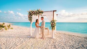 Cerimônia de casamento na praia com um arco branco e decorações florais.