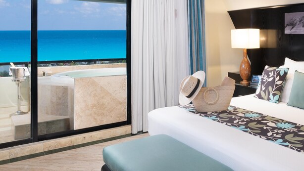 A hotel room with a large balcony, a bed with a patterned bedspread, and a view of the ocean. - The Pyramid Cancun by Oasis - Gourmet Premium All Inclusive (Cancun)