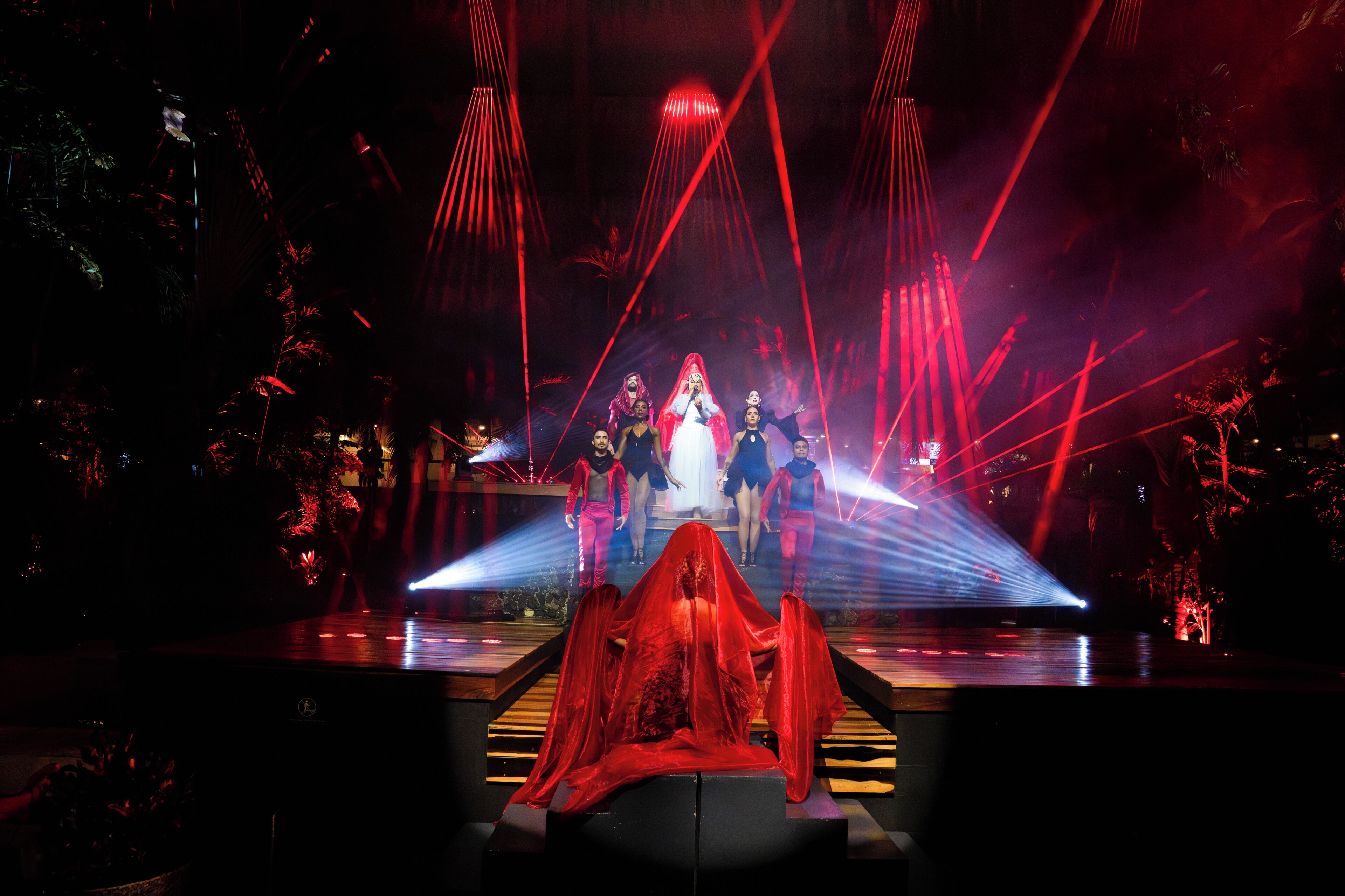 A stage with a group of people in performance attire, a red curtain, and a spotlight.