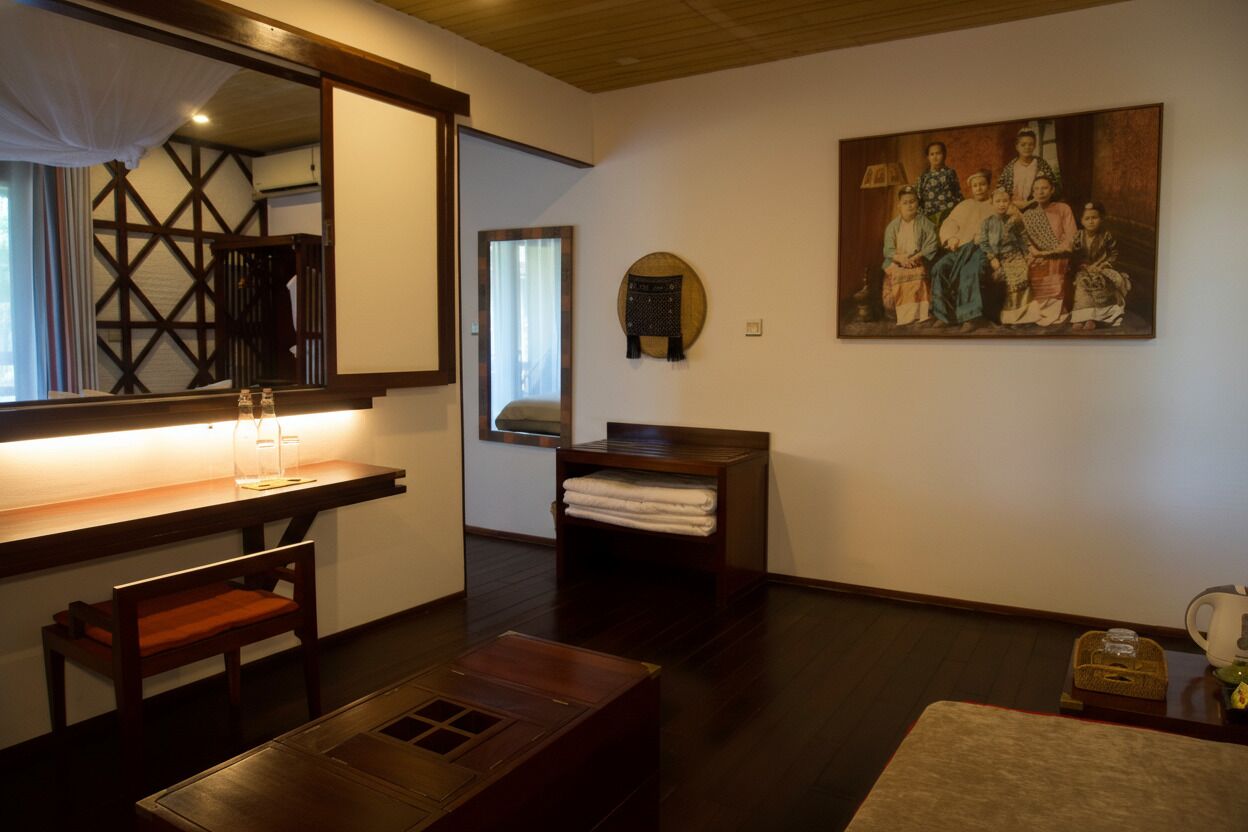 Um quarto japonês tradicional com tatames, uma mesa de madeira baixa, um banco almofadado, um espelho, uma prateleira com toalhas e um retrato de família.