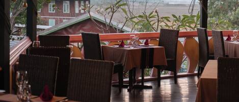 An outdoor dining area with tables and chairs, a view of a building in the background, and a wooden deck.