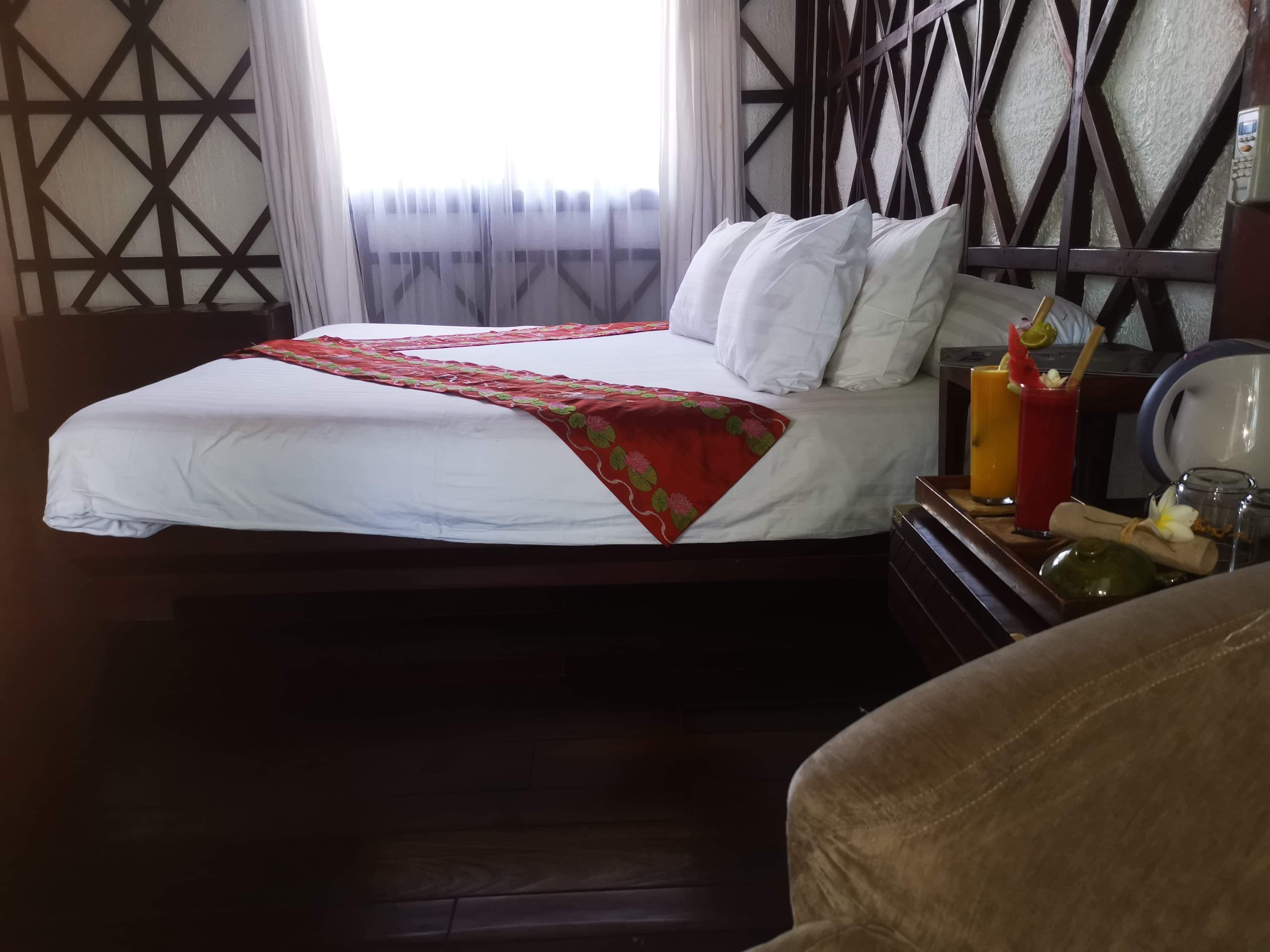 A neatly made bed with a white and red bedspread, a wooden headboard, and a bedside table with a glass of juice and a bottle.