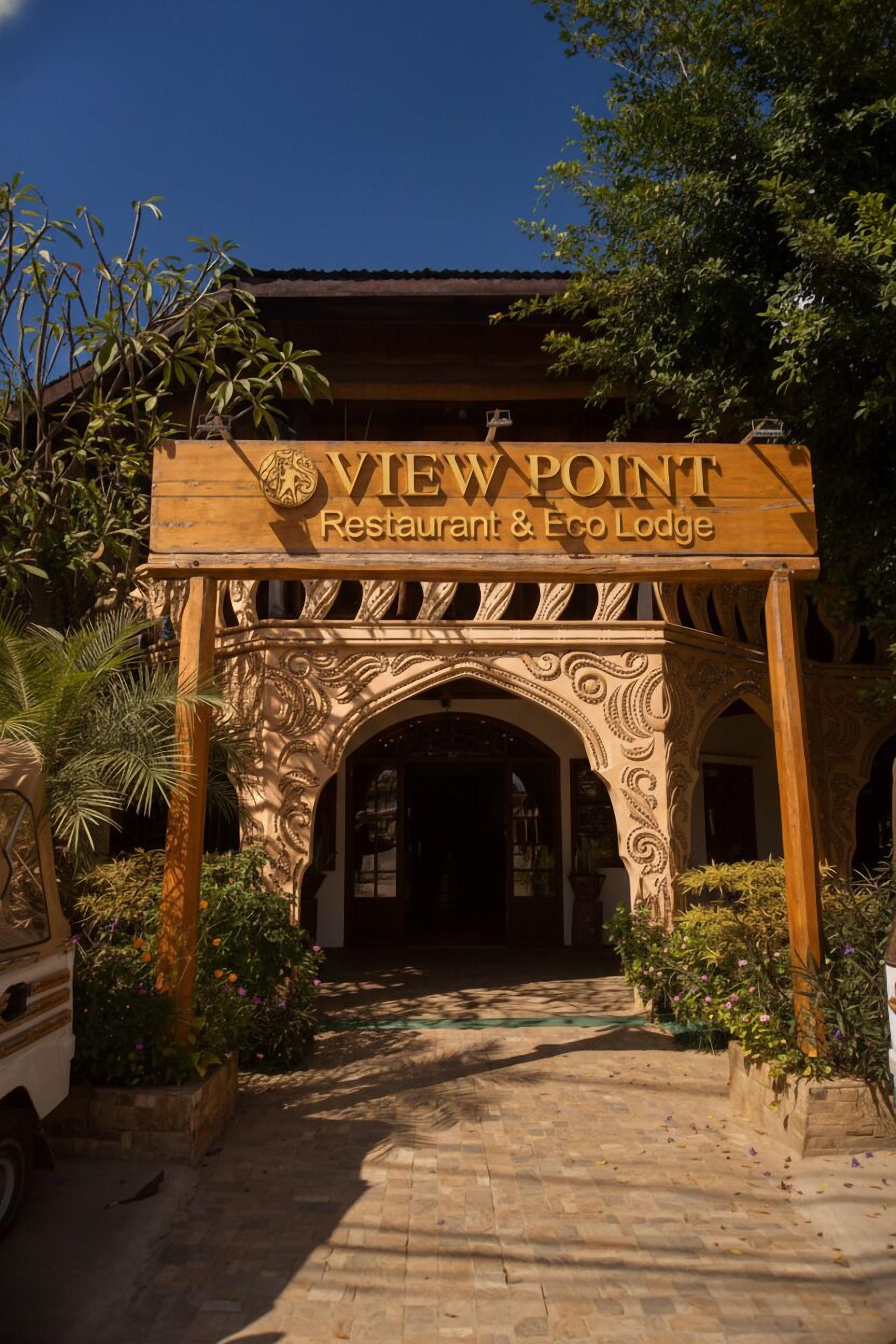A wooden sign with "VIEW POINT Restaurant & Eco Lodge" written on it, an ornate archway, and a pathway leading to the entrance.