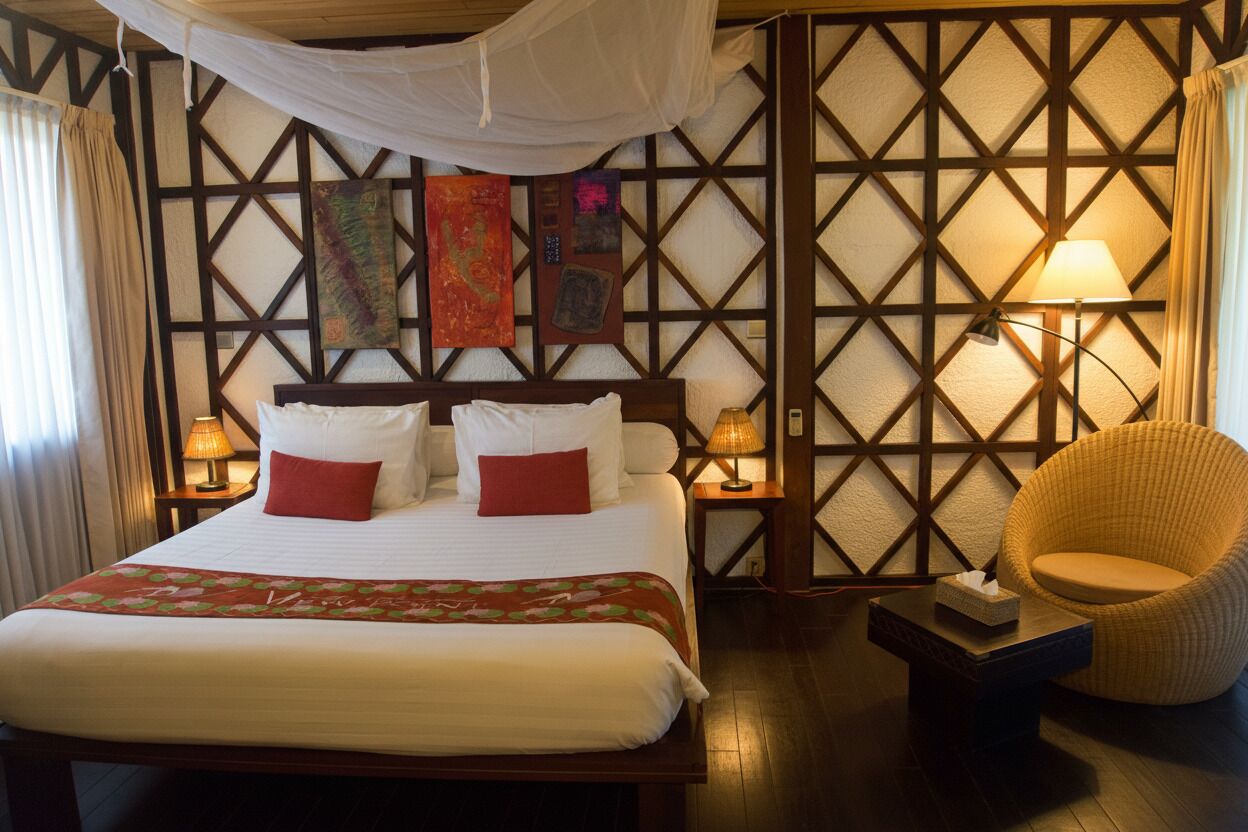 Une chambre d’hôtel avec un grand lit, deux lampes de chevet, une chaise et un mur orné d’un motif géométrique.