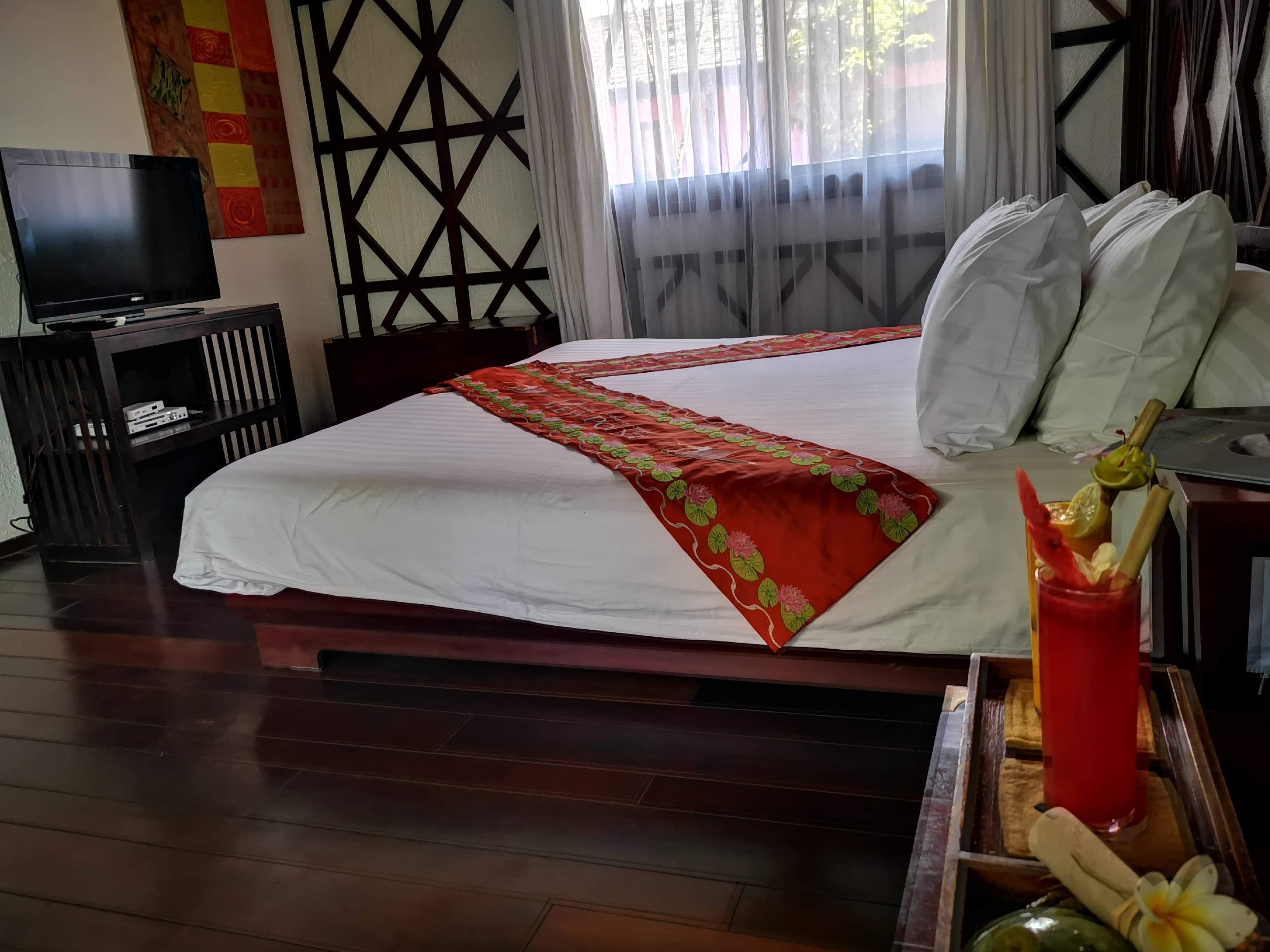 A hotel room with a bed, a television, a wooden cabinet, and a window with curtains.